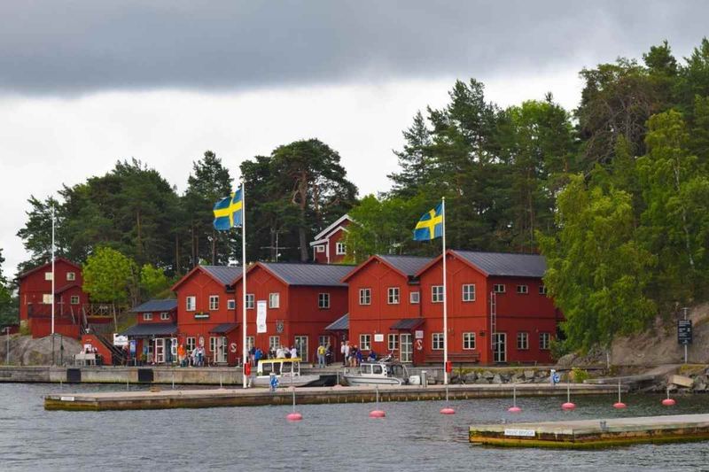 Red wooden buildings with Swedish flags along the quay at Fjäderholmarna