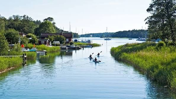 Kayakers paddling along a reed-lined channel past houses and moored boats on Utö