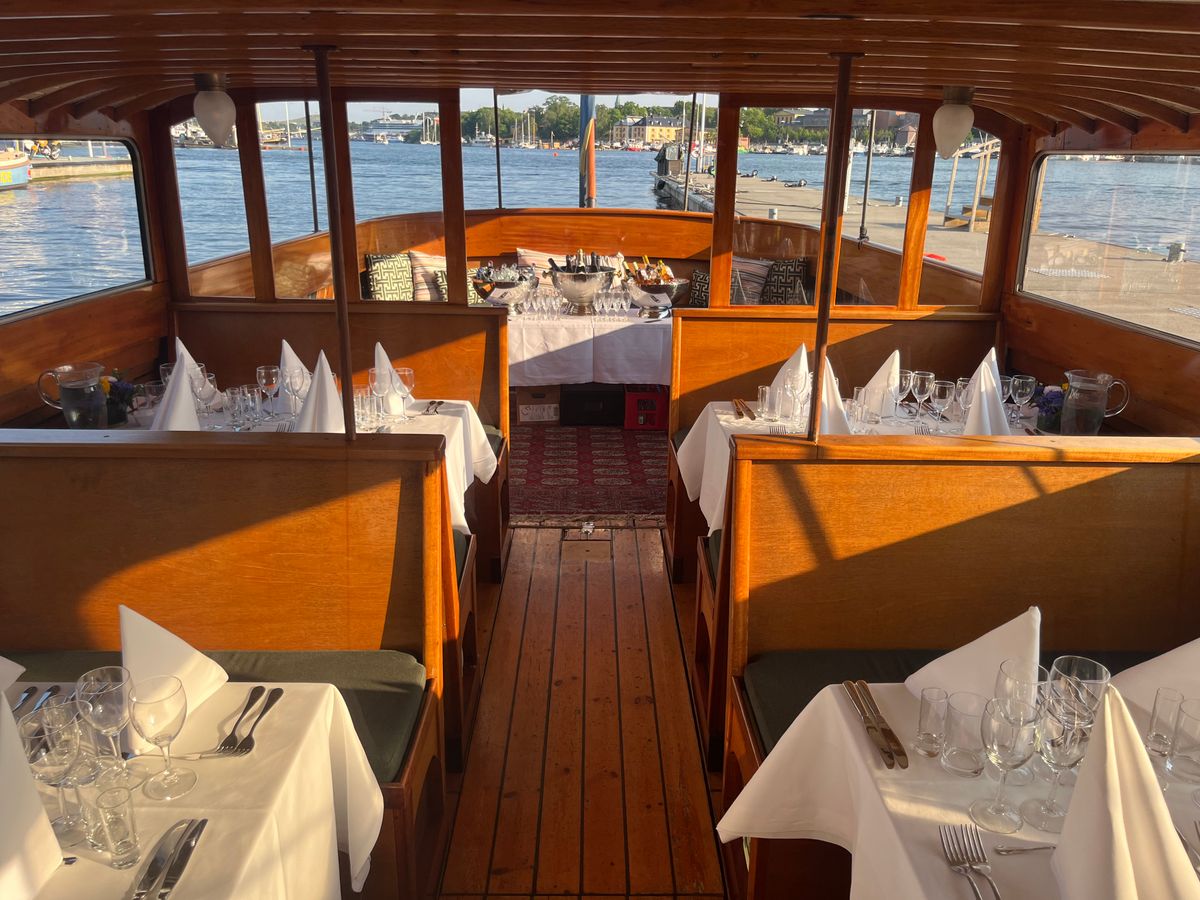 Tables laid with white linen in the wooden salon of the classic boat Sara, ready for a birthday celebration in Stockholm